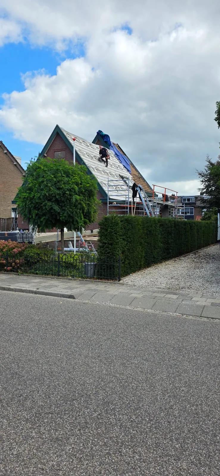 Dakdekker op een steil dak van een bakstenen woning waar de oude pannen af zijn en nieuwe isolatieplaten liggen, met steiger en ladder