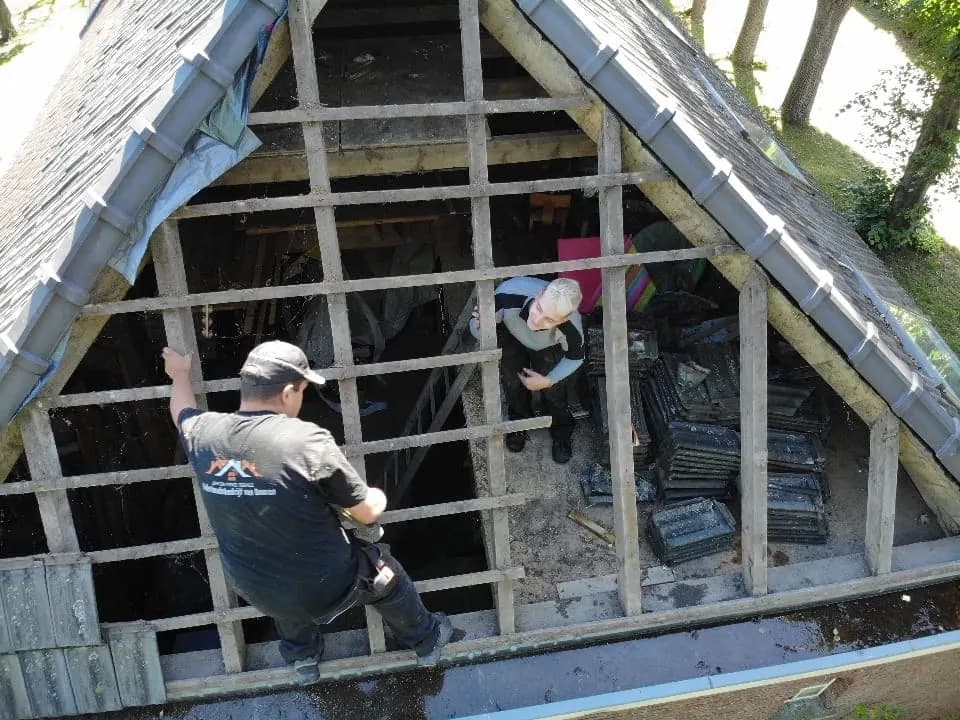 Twee vakmensen tussen nieuwe panlatten op een kap waar de oude pannen af zijn
