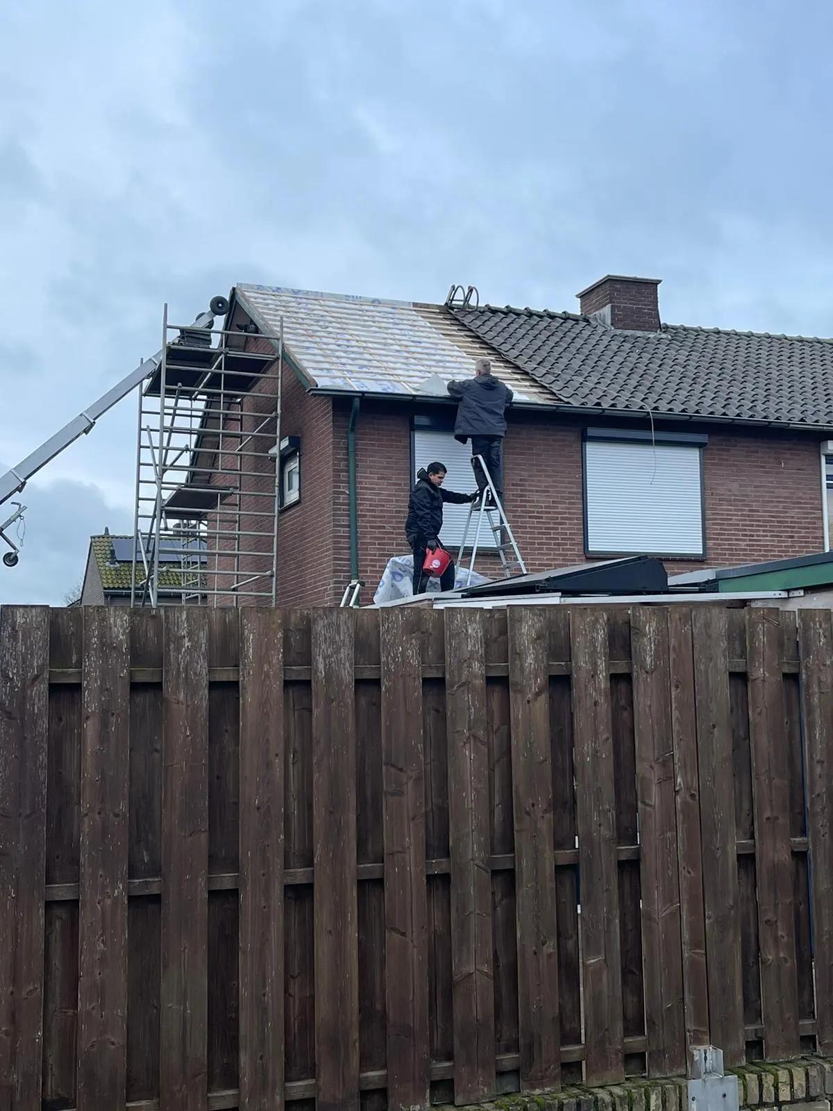 Dakdekkers op steiger en ladder bij een bakstenen twee-onder-een-kapwoning tijdens het vernieuwen van het dak