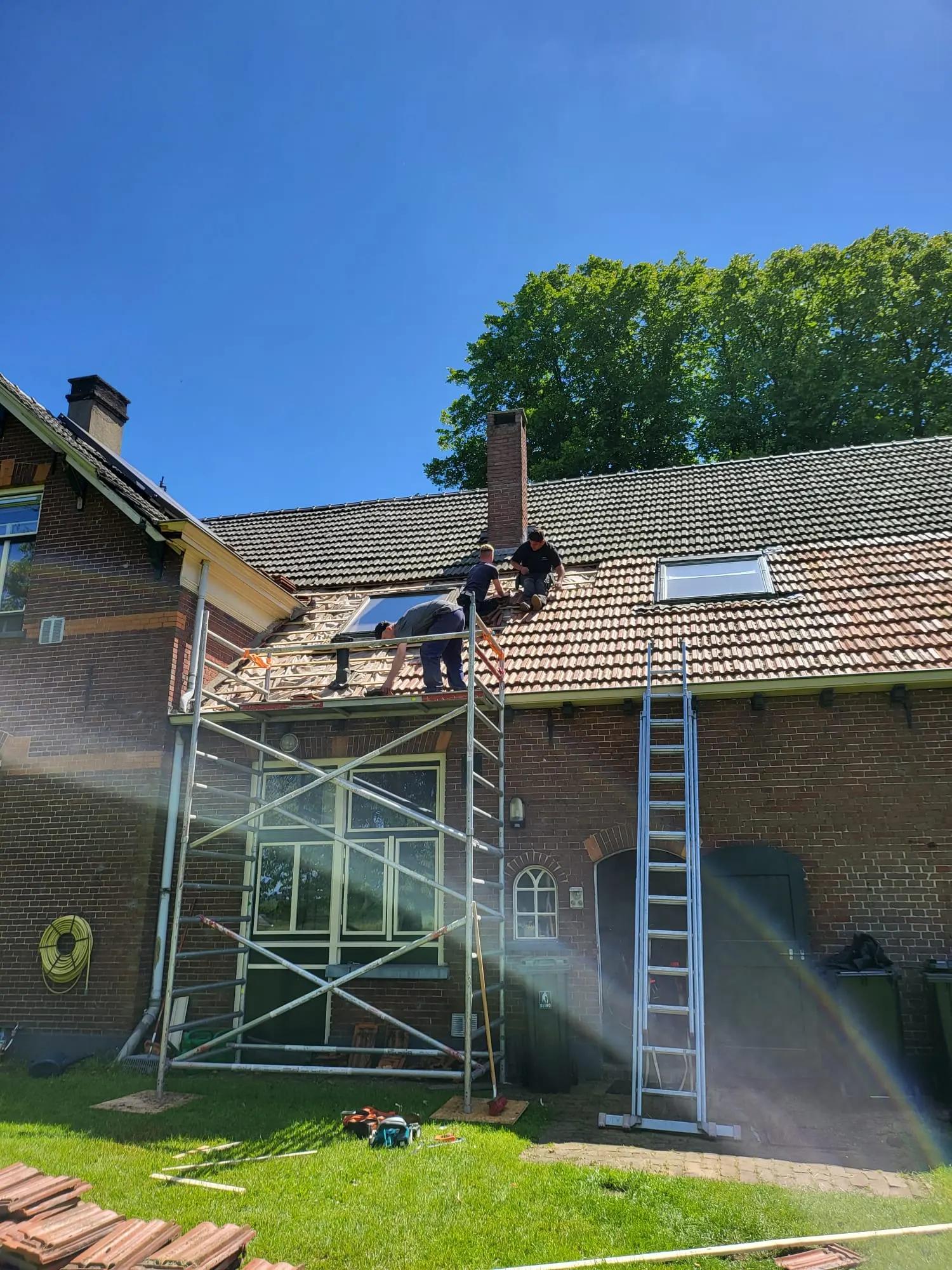 Dakdekkers op het dak van een woonboerderij, met steiger, ladder en oude dakpannen in de tuin