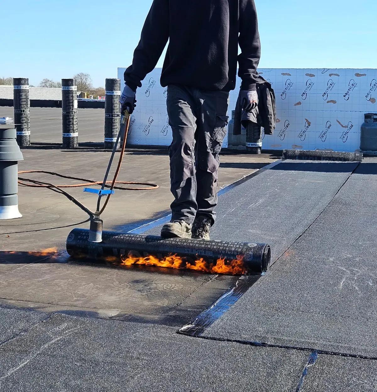 Dakdekker brandt een rol bitumen dakbedekking op een plat dak met een gasbrander