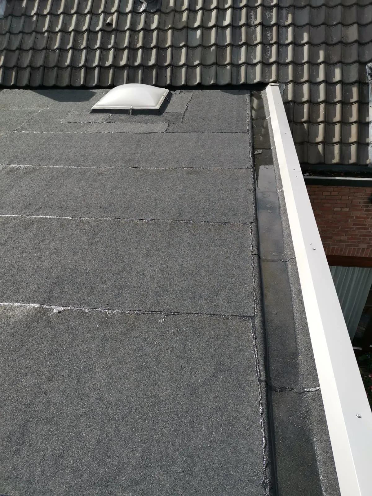 Plat dak met nieuwe bitumen dakbedekking, een lichtkoepel en witte daktrim