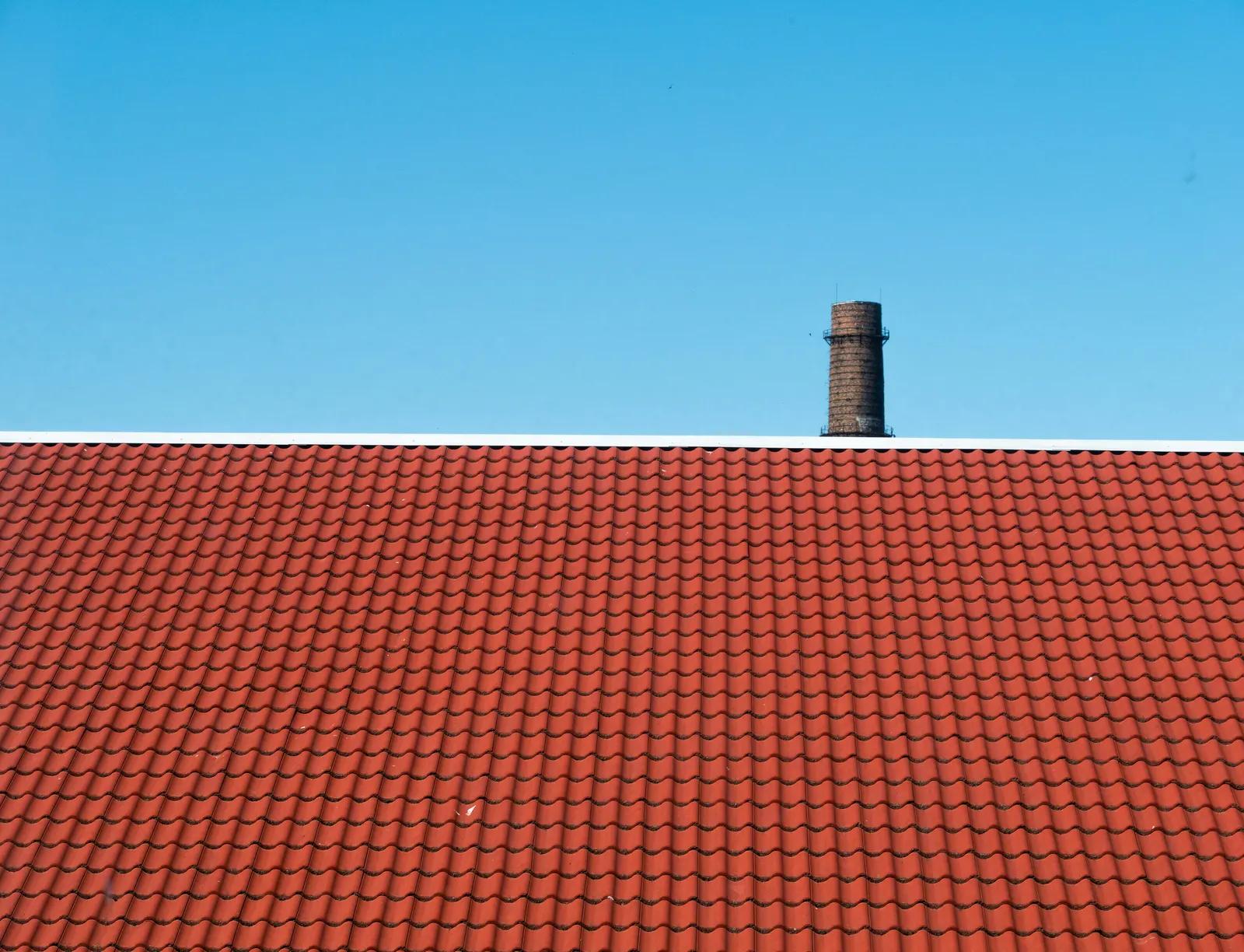 Rood pannendak met een bakstenen schoorsteen tegen een blauwe lucht