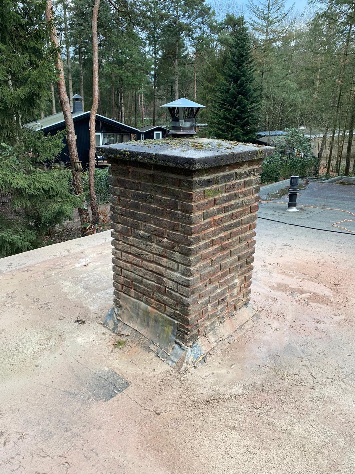 Bakstenen schoorsteen op een plat dak met verweerd metselwerk en mos, voor de renovatie